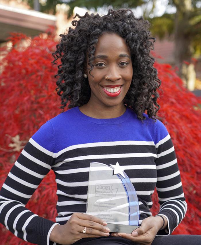 Latoya reid with an award in front of a tree near building F1